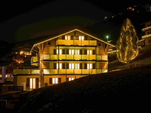 Een meerhoog gebouw met balkons, verlichte ramen en een boom versierd met lichtjes.