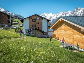 A residential area with wooden houses, a playground, and a mountain backdrop. - Lunic, AZapartments.ch, B&B, (Grächen), 1057 by Interhome (Grächen)
