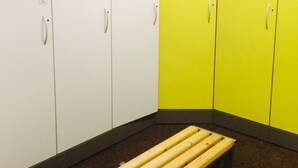 Ein Umkleideraum mit weißen und gelben Schließfächern, einer Bank und einem gefliesten Boden.