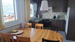 Een keuken met een eettafel en stoelen, een raam met gordijnen, en een hanglamp.