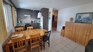 Een eethoek met een houten tafel en stoelen, een keuken op de achtergrond en een televisie op een kast.