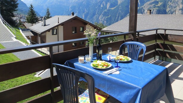 Een balkon met een eettafel voor twee, met uitzicht op een berglandschap.