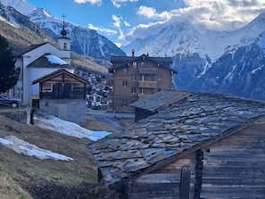 Ein Bergdorf mit traditionellen Holzhäusern, einer Kirche und schneebedeckten Bergen im Hintergrund.