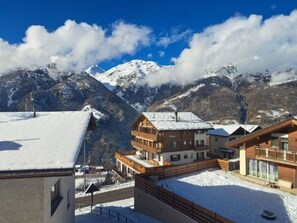 Ein Bergurlaubsort mit schneebedeckten Dächern, Holzhäusern und Blick auf verschneite Gipfel.