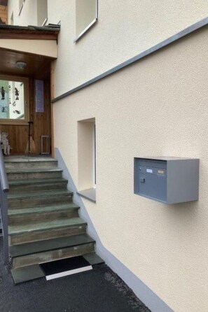 A staircase leading to a building entrance with a wall-mounted electrical box. - Residence Fewo SARAH, (Grächen), 2031 by Interhome (Grächen)