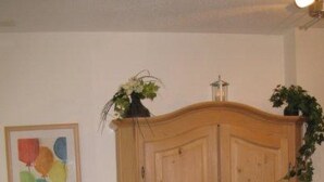 Een houten garderobe met twee deuren, een kunstwerk in een lijst aan de muur, en een plant erop.