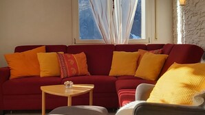 A living room with a red sofa, a small round table, and a view of mountains through a window. - Silberblick, (Grächen), by Interhome (Grächen)