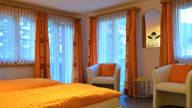 Habitación de hotel con cama, dos sillones, una mesita y cortinas.