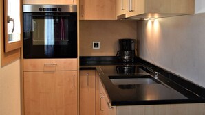 Una cocina compacta con armarios de madera, una encimera negra y un horno empotrado.