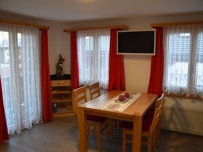 A dining area with a wooden table, chairs, and a TV mounted on the wall. - Ferienwohnungen Zur Heimat, (Grächen), by Interhome (Grächen)