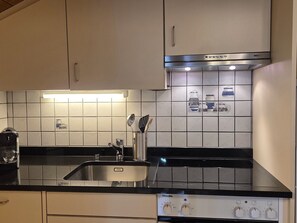 Eine Küche mit schwarzem Arbeitsplatz, Edelstahlgeräten und einer gefliesten Spritzschutzwand.