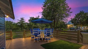 A deck with outdoor furniture and a blue umbrella, surrounded by a wooden fence and trees. - Sunnyside Creek House | Hidden Inlet Escape Est'38 (Murrells Inlet)