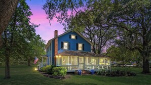 A two-story house with a covered porch, surrounded by trees and a well-maintained lawn. - Sunnyside Creek House | Hidden Inlet Escape Est'38 (Murrells Inlet)