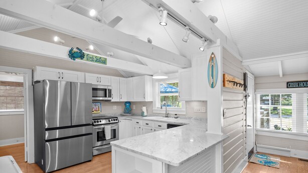 A modern kitchen with white cabinetry, stainless steel appliances, and a marble countertop. - Sunnyside Creek House | Hidden Inlet Escape Est'38 (Murrells Inlet)