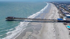 A beach with a pier extending into the ocean, a sandy beach, and buildings along the shore. - Sunnyside Creek House | Hidden Inlet Escape Est'38 (Murrells Inlet)