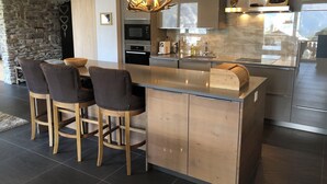 Een moderne keuken met een centraal eiland, barstoelen, een stenen muur en een kroonluchter.