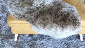 Een gele sofa met tuftbekleding, twee gele kussens en een bont plaid op een grijs vloerkleed.