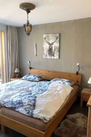 Un dormitorio con una cama de madera, una lámpara de pared, un cuadro de un ciervo y una ventana con cortinas.