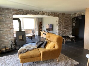 A cozy living room with a stone wall, a fireplace, a sofa, and a TV. - Morion, Haus Alana, (Grächen), by Interhome (Grächen)