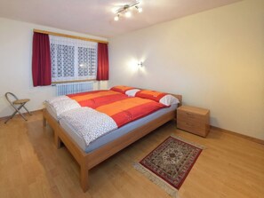 Ein Schlafzimmer mit Bett, Nachttisch, Sessel, einem Fenster mit Vorhängen und einer Stehlampe.