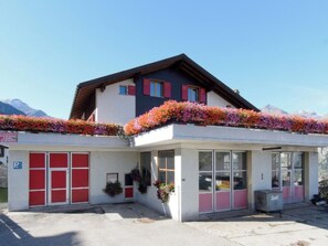 Ein Gebäude mit einem geneigten Dach, einer Garage mit roten Türen und einer mit Blumen bepflanzten Fassade.