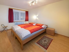 A bedroom with a wooden bed, a nightstand, a chair, a window with curtains, and a radiator. - Ferienwohnungen Schmiedstube 420, (Grächen), by Interhome (Grächen)