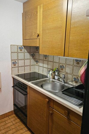A kitchen with wooden cabinets, a stainless steel sink, and a tiled backsplash. - Nr.25,Haus Azurit, (Grächen), 1010 by Interhome (Grächen)