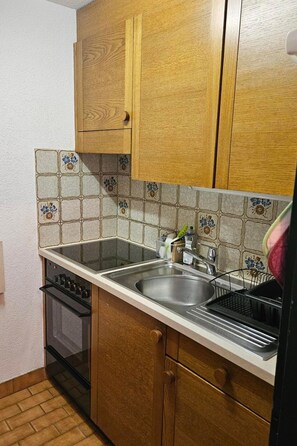 Eine Küche mit Holzausstattung, einer gefliesten Spritzschutzwand, einer Edelstahl-Spüle und einem eingebauten Ofen.