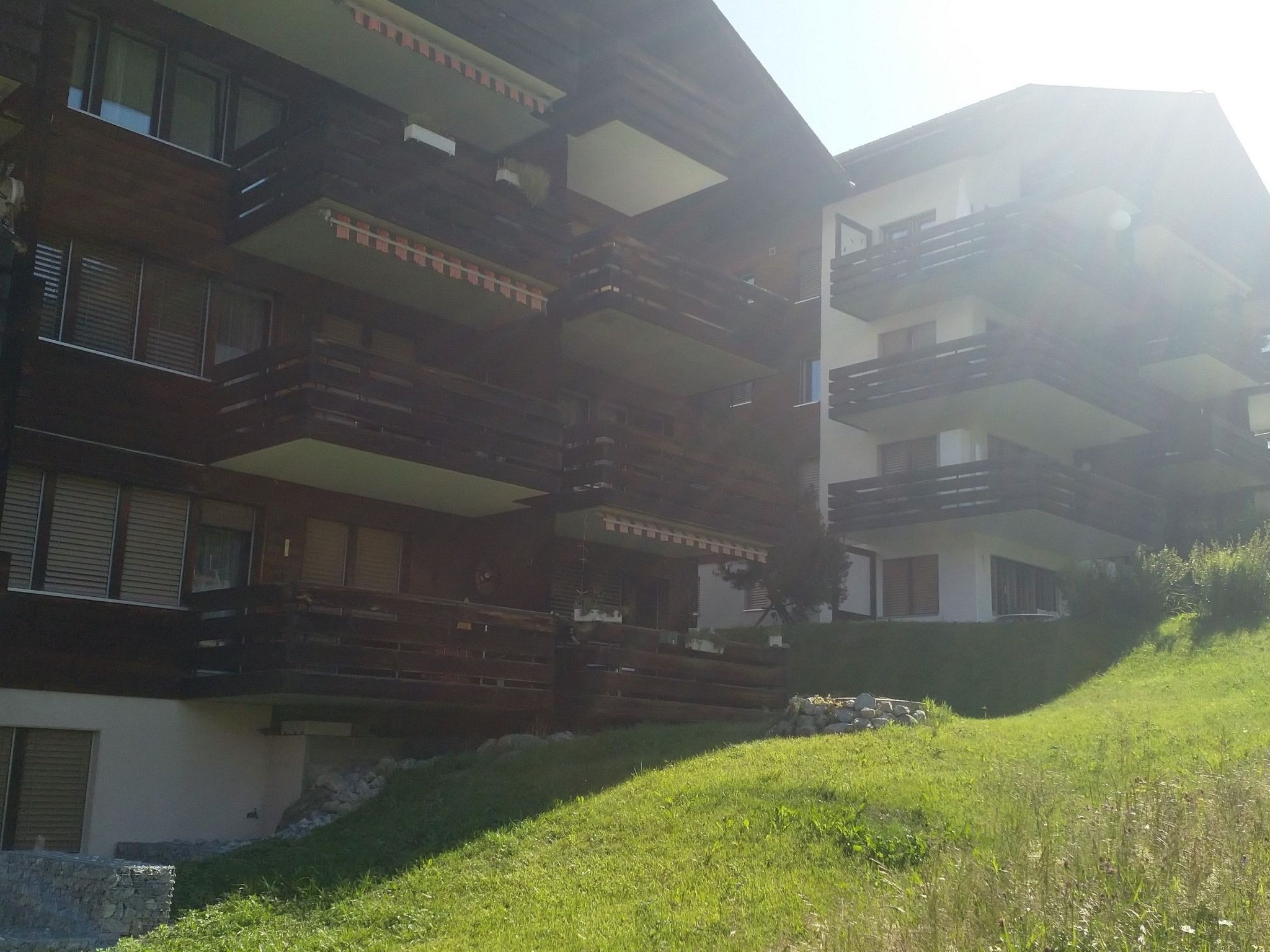 Un edificio a più piani con balconi, una base in pietra e un pendio erboso.