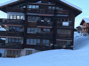 A multi-story wooden building with balconies, likely a hotel or lodge, surrounded by snow. - Nr.25,Haus Azurit, (Grächen), 1010 by Interhome (Grächen)