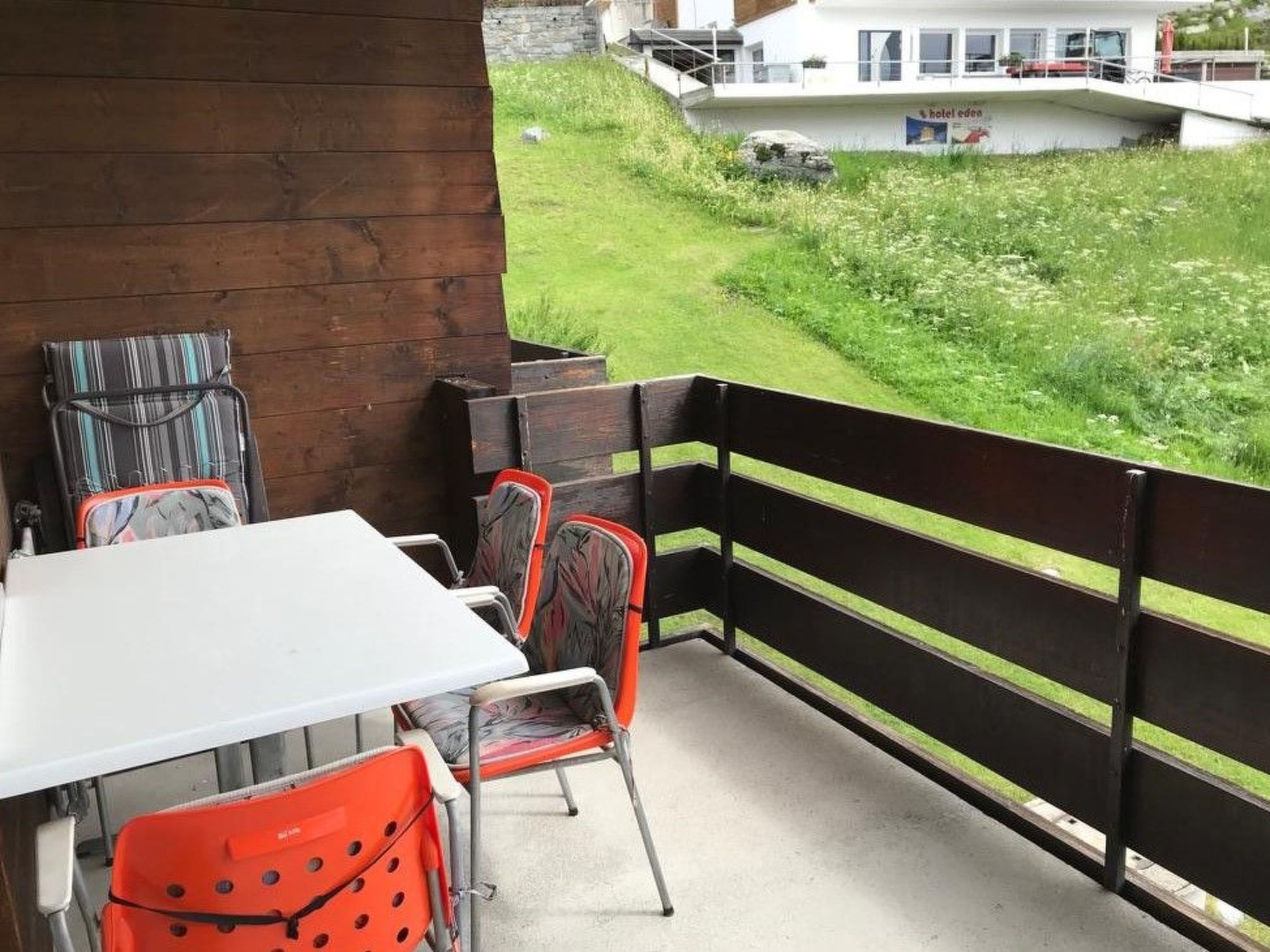 Un balcón con mesa y sillas, con vistas a un área verde y un edificio con un cartel.