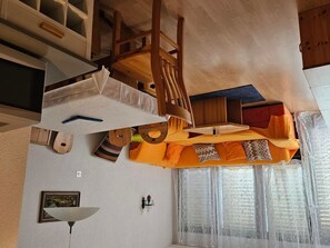 Ein Zimmer mit einem Bett, einem Schreibtisch, einem Sessel, einem Fenster mit Vorhängen und einer Wandlampe.