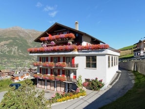 A two-story building with balconies adorned with flowers, set against a mountainous backdrop. - Ferienwohnungen Schmiedstube 420, (Grächen), by Interhome (Grächen)