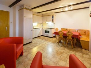 A compact kitchen with white cabinets, a dining table with four chairs, and a red sofa. - Ferienwohnungen Schmiedstube 420, (Grächen), by Interhome (Grächen)