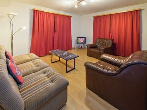 Ein Wohnzimmer mit einer Couch, einem Ledersessel, einem Couchtisch und einem Fernseher.