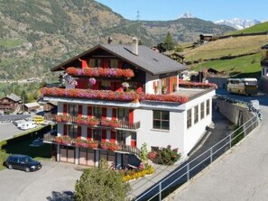 A multi-story building with balconies adorned with flowers, set against a mountainous backdrop. - Ferienwohnungen Schmiedstube 420, (Grächen), by Interhome (Grächen)
