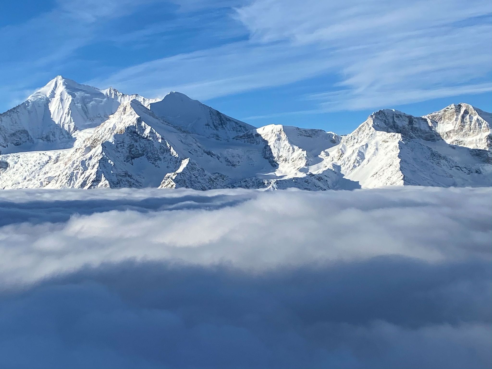 Eine Bergkette mit schneebedeckten Gipfeln und einer Wolkenschicht darunter.