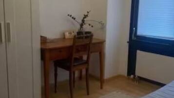 A bedroom with a bed, a desk, and a chair. There is a window with blinds.