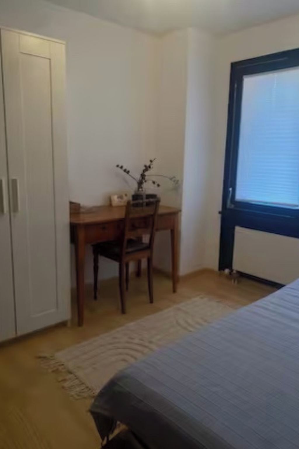 A bedroom with a bed, a wooden desk, a chair, and a window.