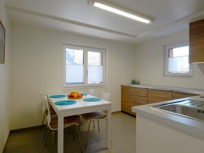 Eine kleine Küche mit Esstisch, Stühlen, Spüle und Fenster.