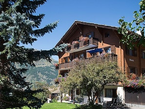 Ein mehrstöckiges Hotel mit Balkonen, Blick auf die Berge und einem gepflegten Garten.