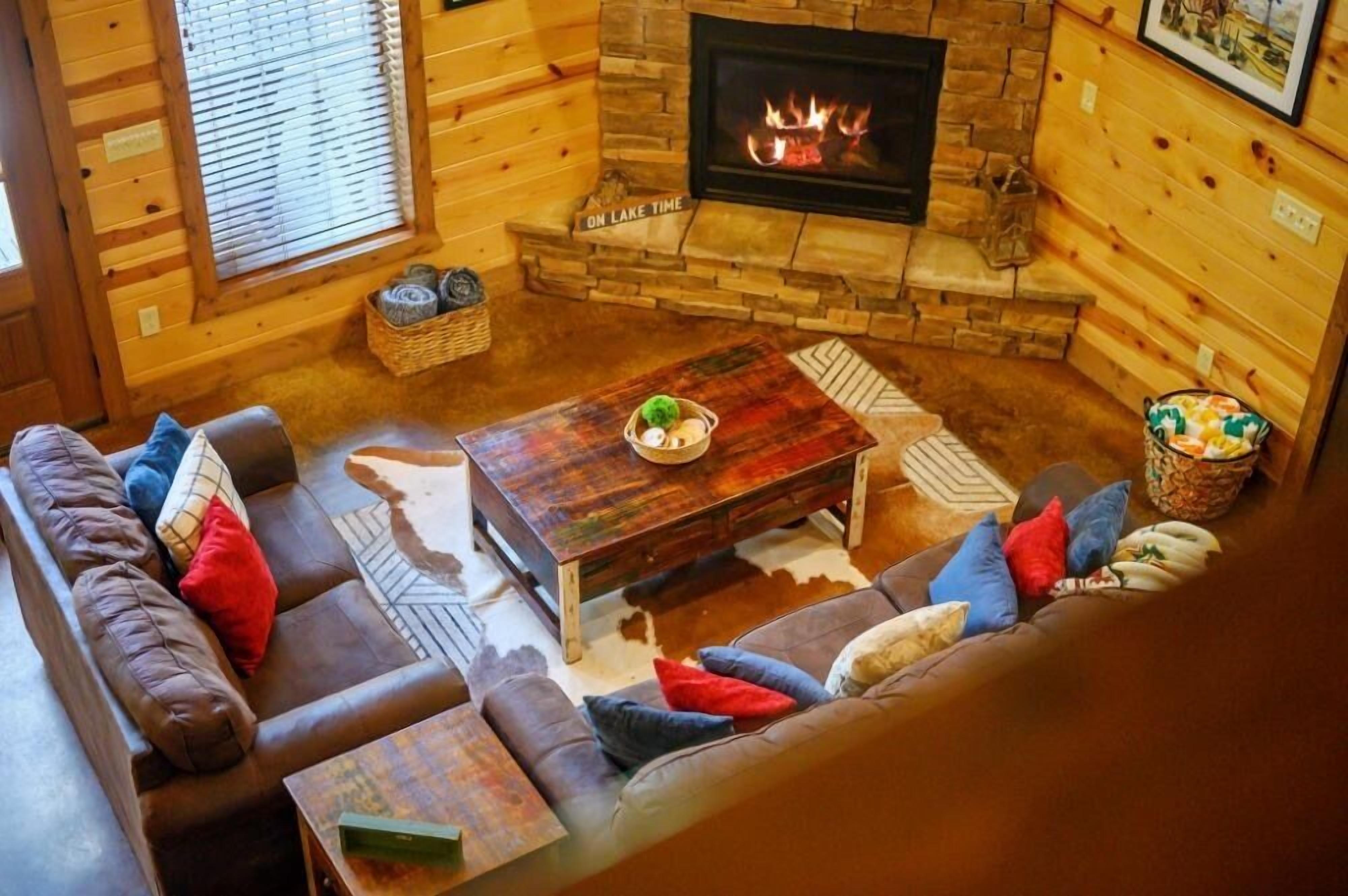L’intérieur d’un chalet chaleureux, avec une cheminée en pierre, des murs en bois, un canapé en cuir et une table basse.