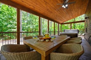 Una terraza de madera con una mesa lista para comer, rodeada de sillas de mimbre, y una parrilla al fondo.
