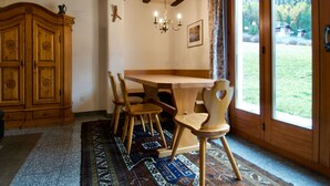 A dining area with a wooden table and chairs, a chandelier, a large wooden cabinet, and a view of a green landscape through a glass door. - Goldblick, (Grächen), 1767+1034+2083 by Interhome (Grächen)