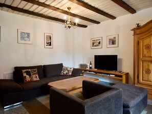 Ein Wohnzimmer mit einer Couch, zwei Sesseln, einem Couchtisch, einem Fernseher und gerahmten Bildern an der Wand.