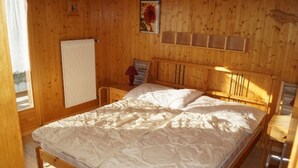 Een kamer met houten lambrisering, een bed, een nachtkastje, een lamp en een raam.