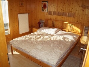 A wooden-paneled room with a bed, a nightstand, a lamp, and a window. - Dilaila, (Grächen), by Interhome (Grächen)