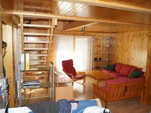 A wooden cabin interior with a wooden desk, bookshelves, a red chair, a wooden sofa, and a dining table. - Dilaila, (Grächen), by Interhome (Grächen)