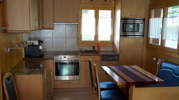 Een compacte keuken met een fornuis, oven, magnetron en een eethoek met een tafel en stoelen.