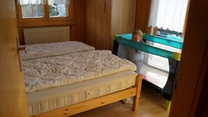 Een houten bed met een matras en een kind bij een raam.